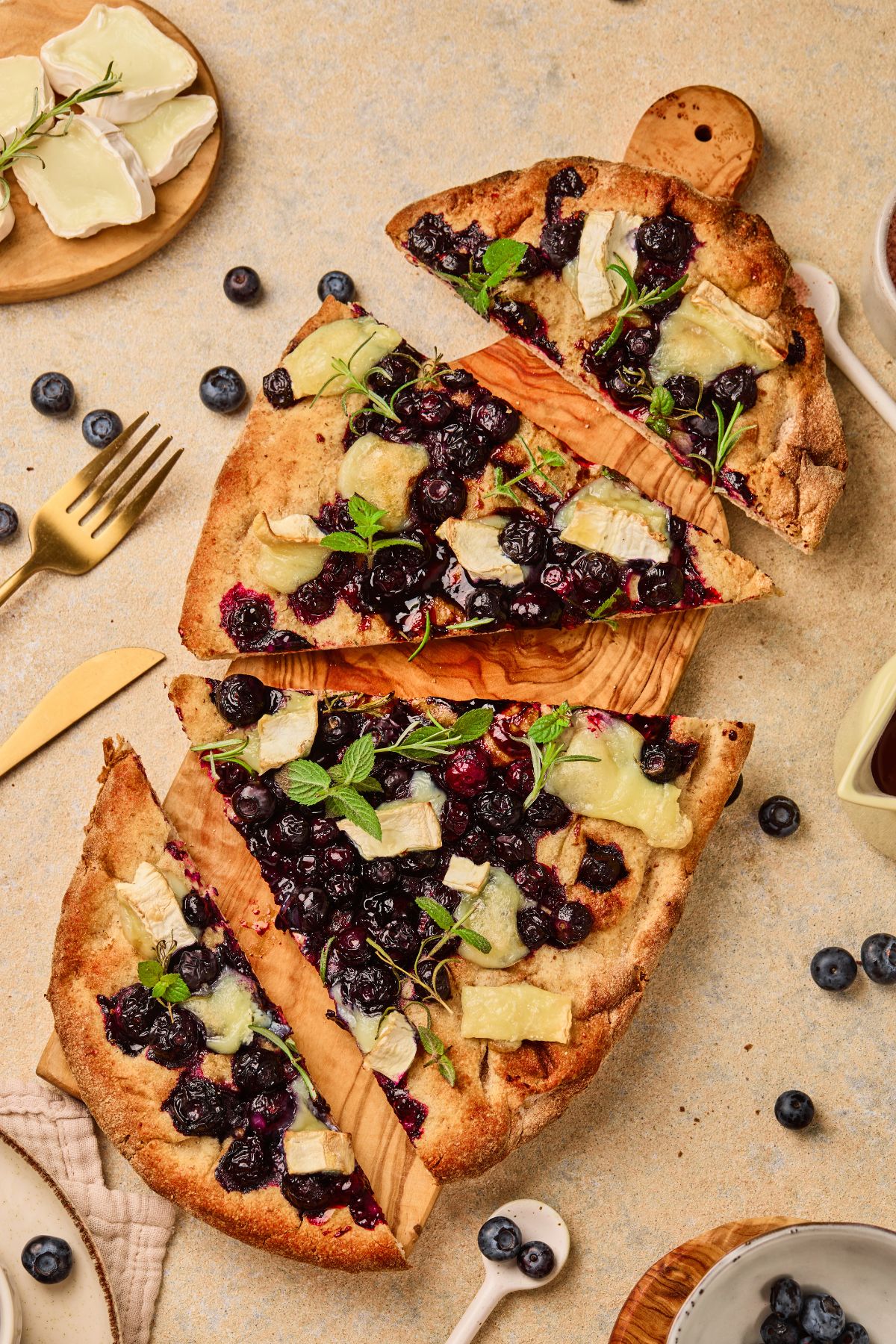 Delicious homemade blueberry and cheese pizza on a wooden board, served with fresh blueberries and herbs.