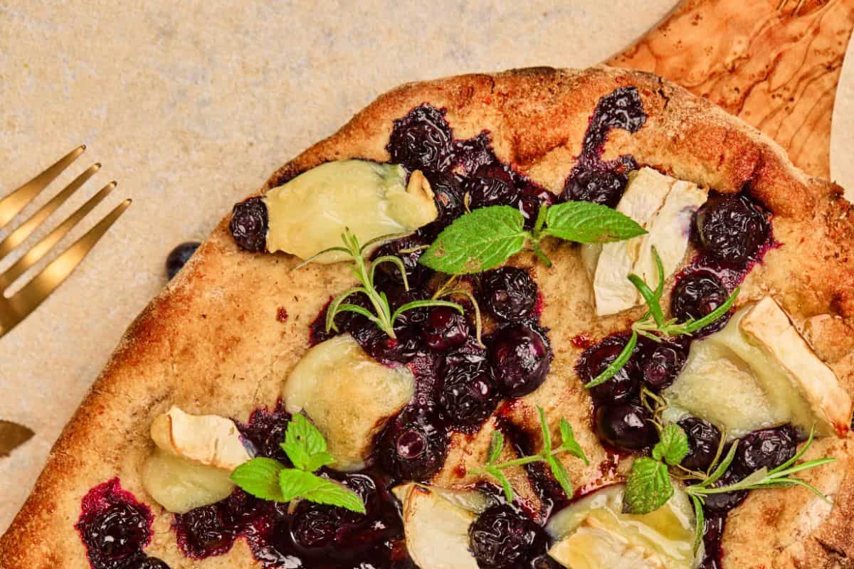 Close-up of a fruity dessert pizza topped with blueberries, cheese, and fresh mint leaves.