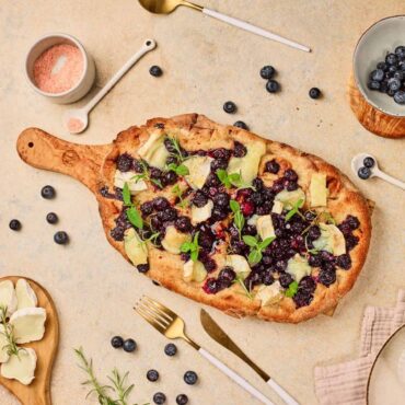 Delicious homemade berry fruit flatbread with cheese and fresh herbs on a rustic platter. Perfect for a sweet, savory snack or meal.