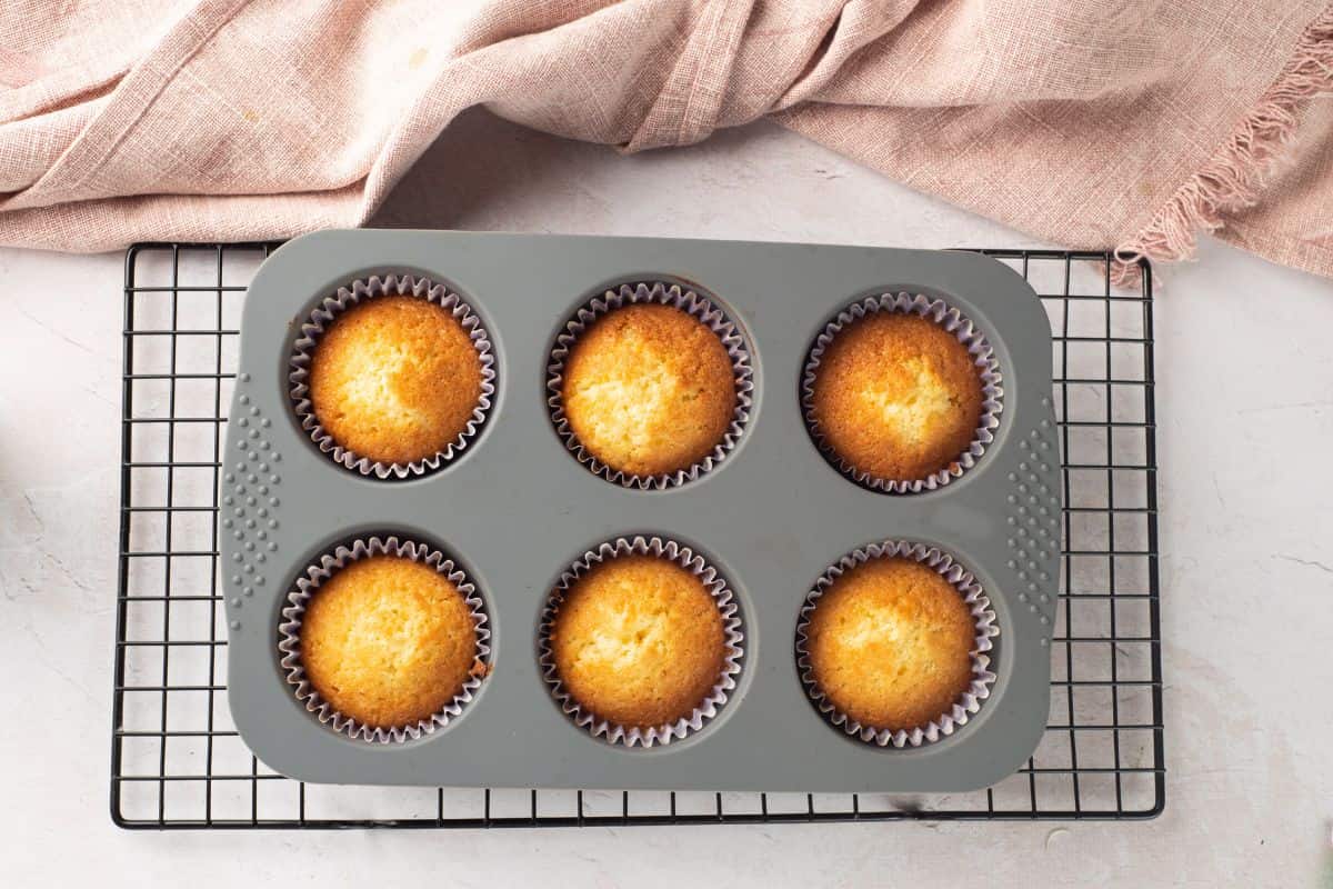 Freshly baked vanilla cupcakes in colorful paper liners cooling on a wire rack.