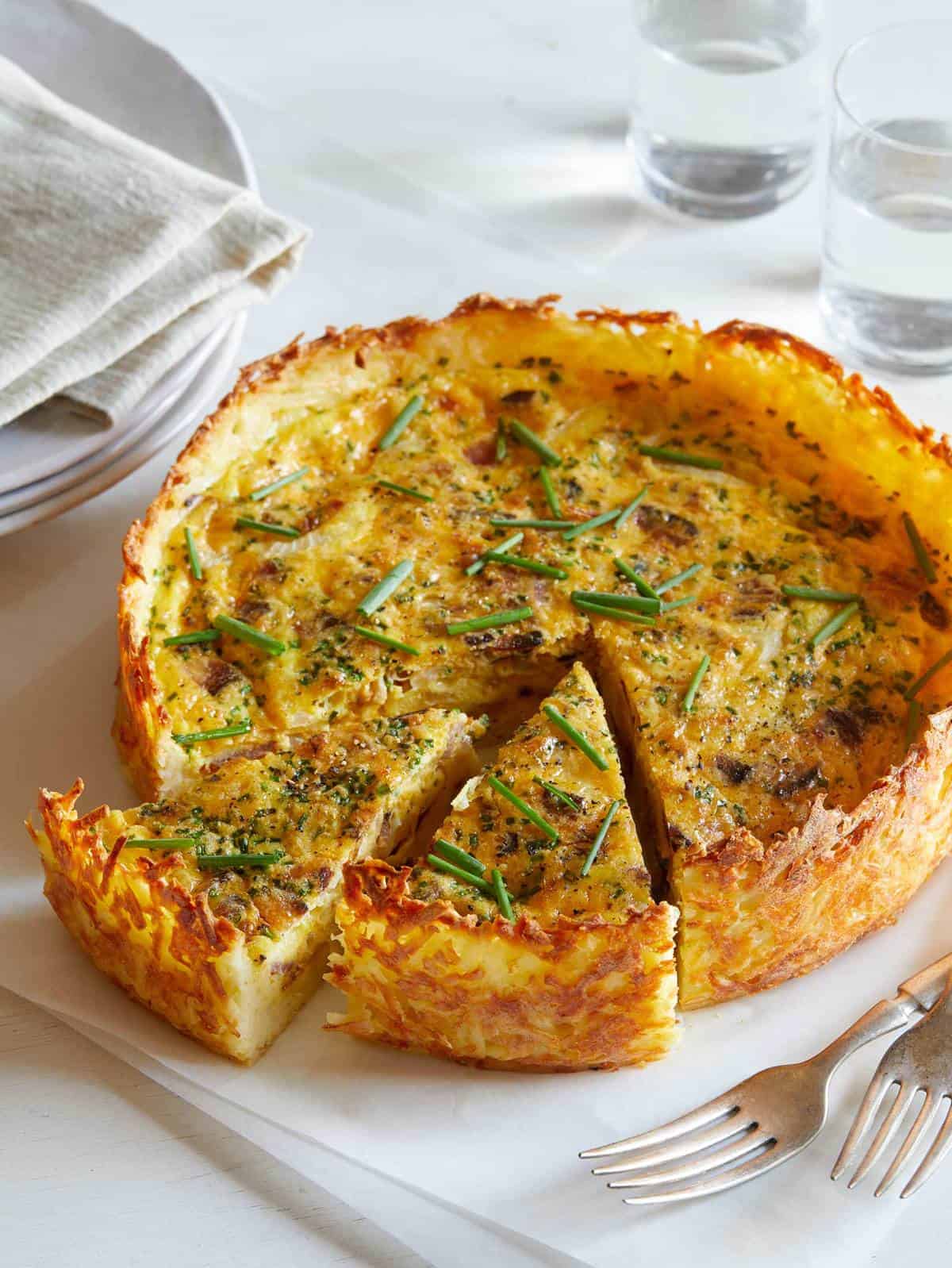 A bacon and onion quiche with a hash brown crust on a platter with two slices out. 