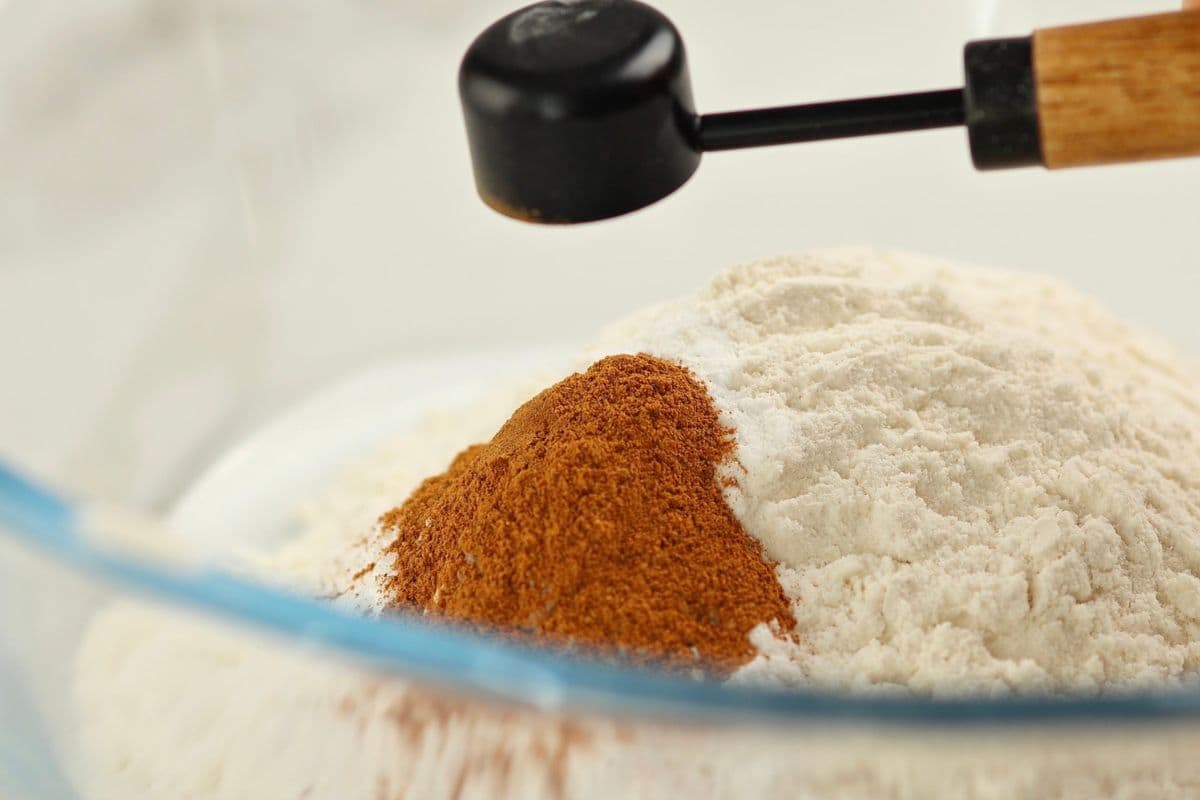 Close-up of cinnamon and flour in a mixing bowl with a baking spoon.