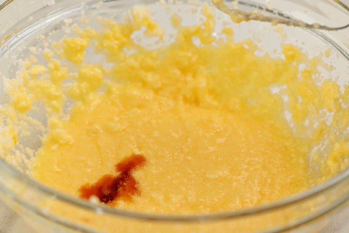 Close-up of a yellow butter and vanilla mixture in a glass bowl, with vanilla extract visible at the bottom.