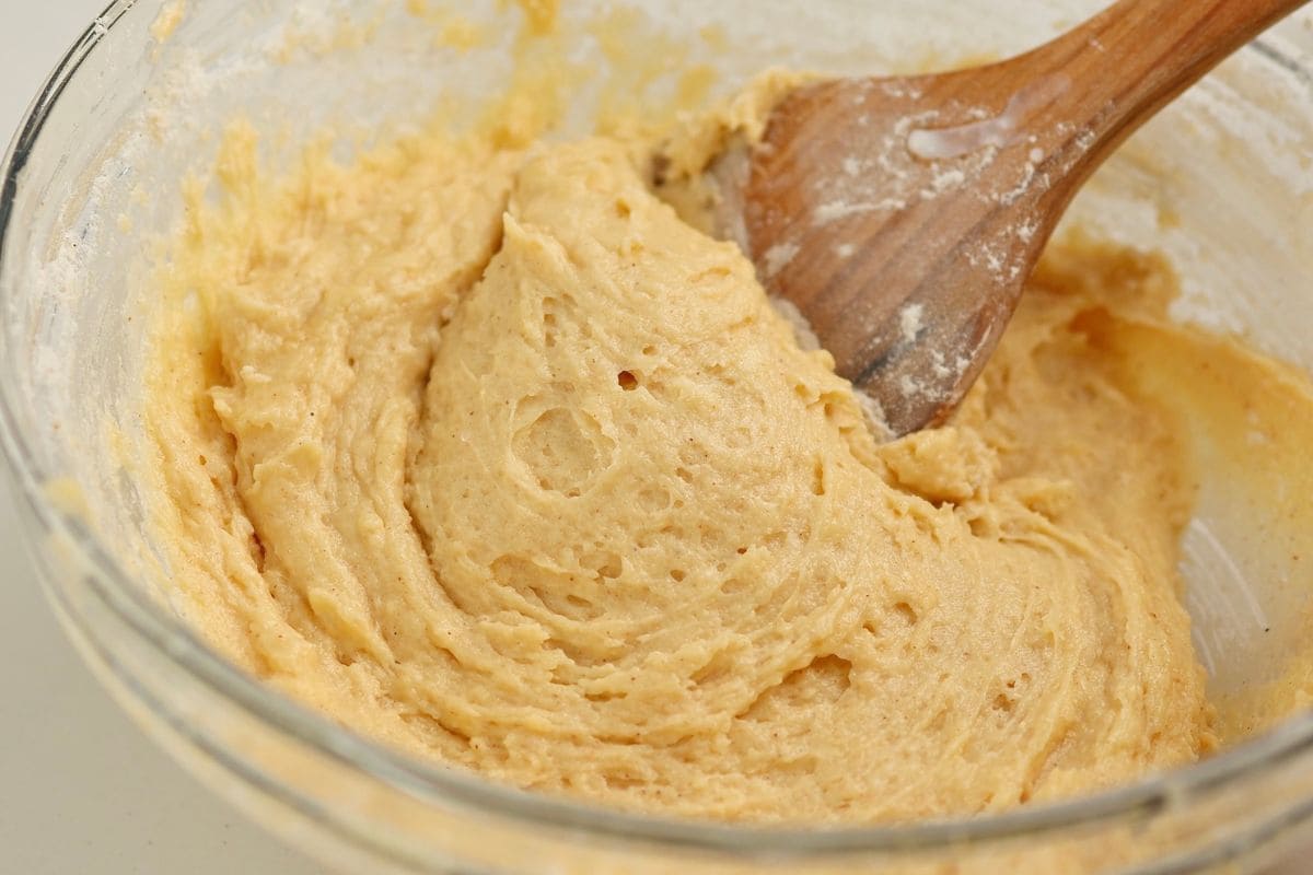 Alt text: Close-up of smooth, creamy batter in a glass bowl with a wooden spoon.